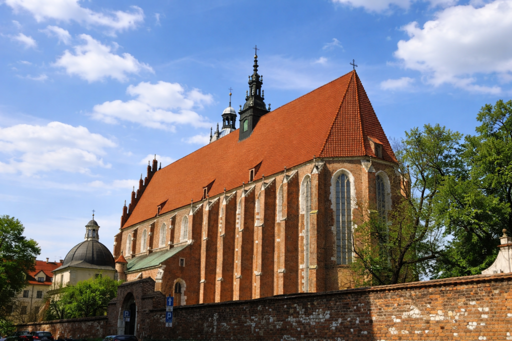 Corpus Christi Basilica in Krakow on a summer day, with red tiled roof and Gothic brick architecture under a lightly cloudy blue sky