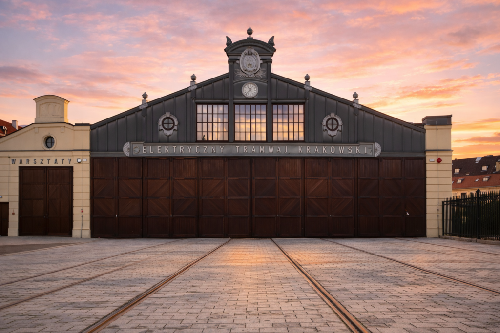 Historic Krakow tram depot building seen from the front at sunset with tram tracks leading towards the entrance.