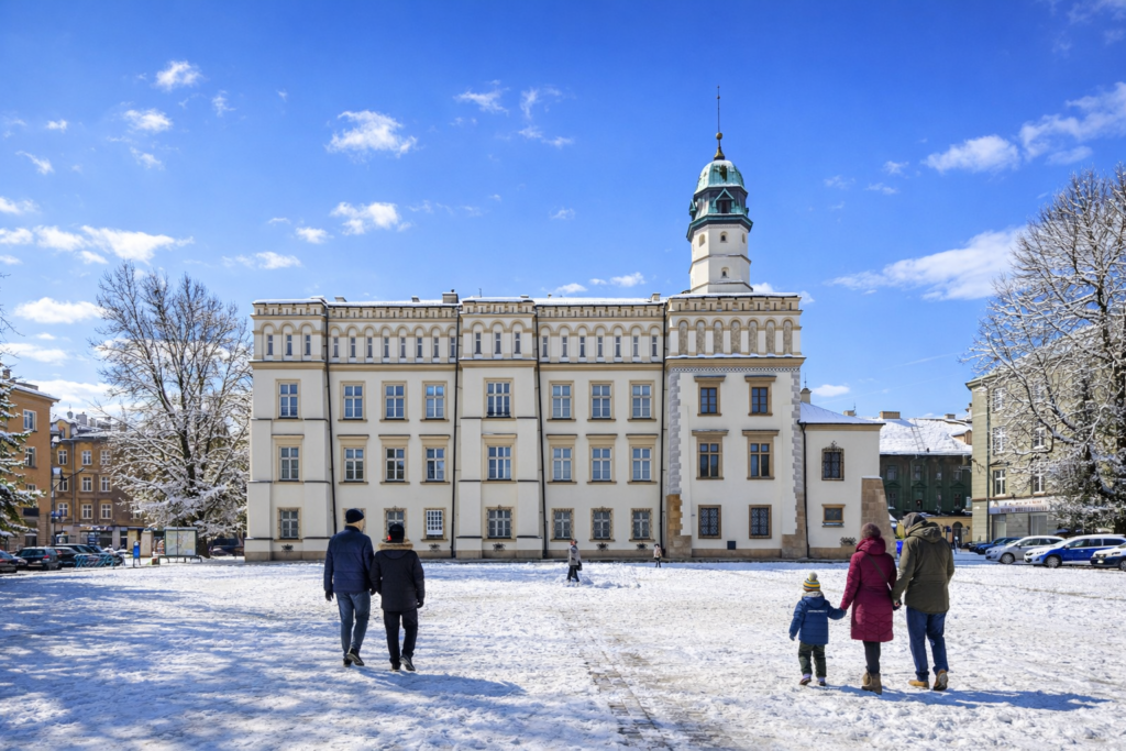 Plac Wolnica in Krakow on a sunny winter day with snow-covered ground and a few people walking across the square.