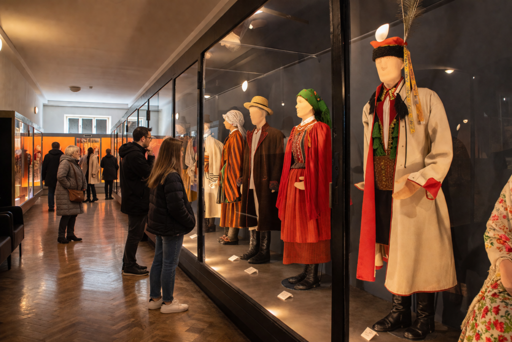 Ethnographic Museum in Krakow interior with traditional folk costumes displayed in glass cases and visitors viewing the exhibition.