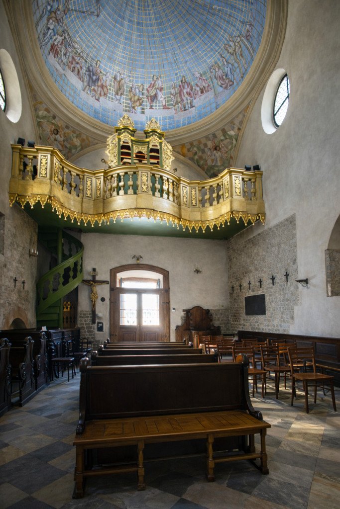 Interior of St. Adalbert’s Church in Krakow’s Main Market Square, with wooden pews, a gilded organ gallery and a painted dome above.