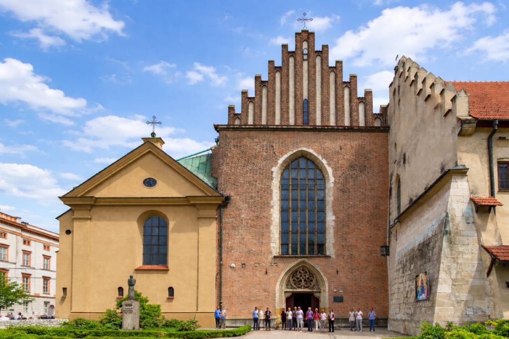 Franciscan Basilica in Krakow opposite the Papal Window, with Gothic brick façade and a smaller chapel beside it under a clear summer sky.