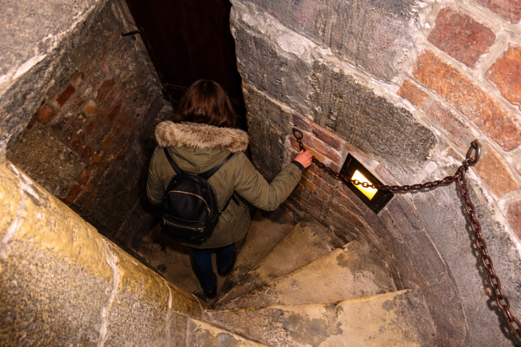 Person descending a narrow spiral staircase inside a historic tower in Krakow.