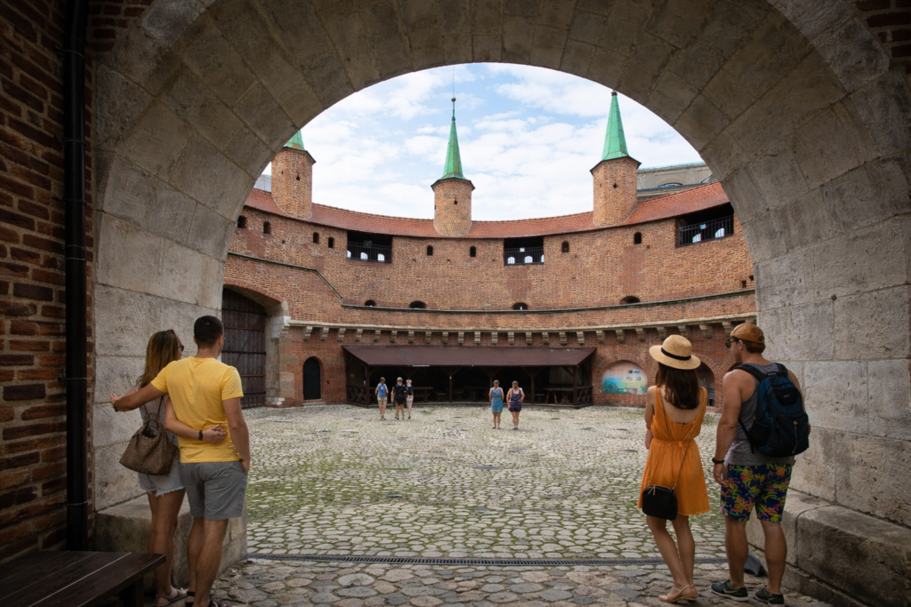 Krakow Barbican interior courtyard viewed through a stone arch with a few tourists exploring the historic fortification.