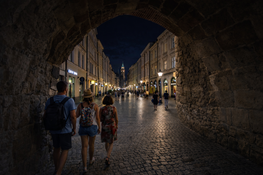 View from inside St. Florian’s Gate in Krakow at night, with tourists walking along Floriańska Street towards the Old Town.