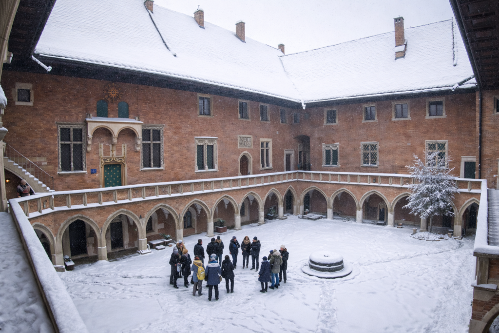 Collegium Maius courtyard in Krakow covered in snow, with historic arcades and visitors gathered around the central well.
