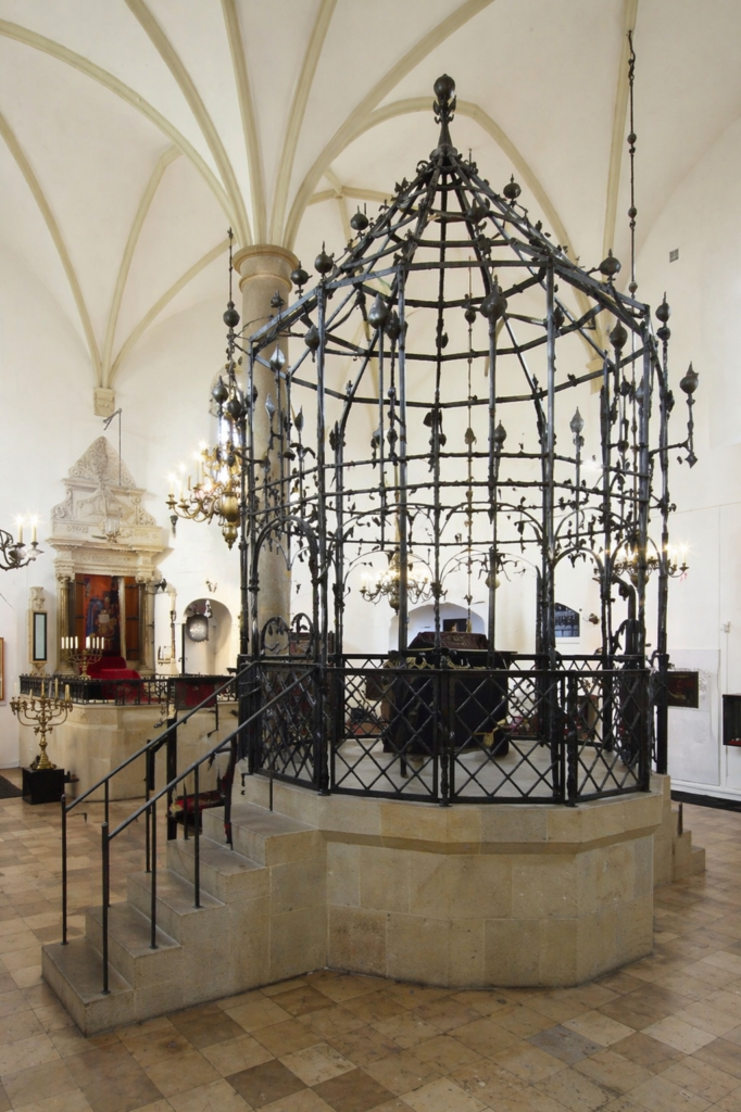 Interior of the Old Synagogue in Krakow with a central iron bimah enclosure, viewed from ground level at close range.
