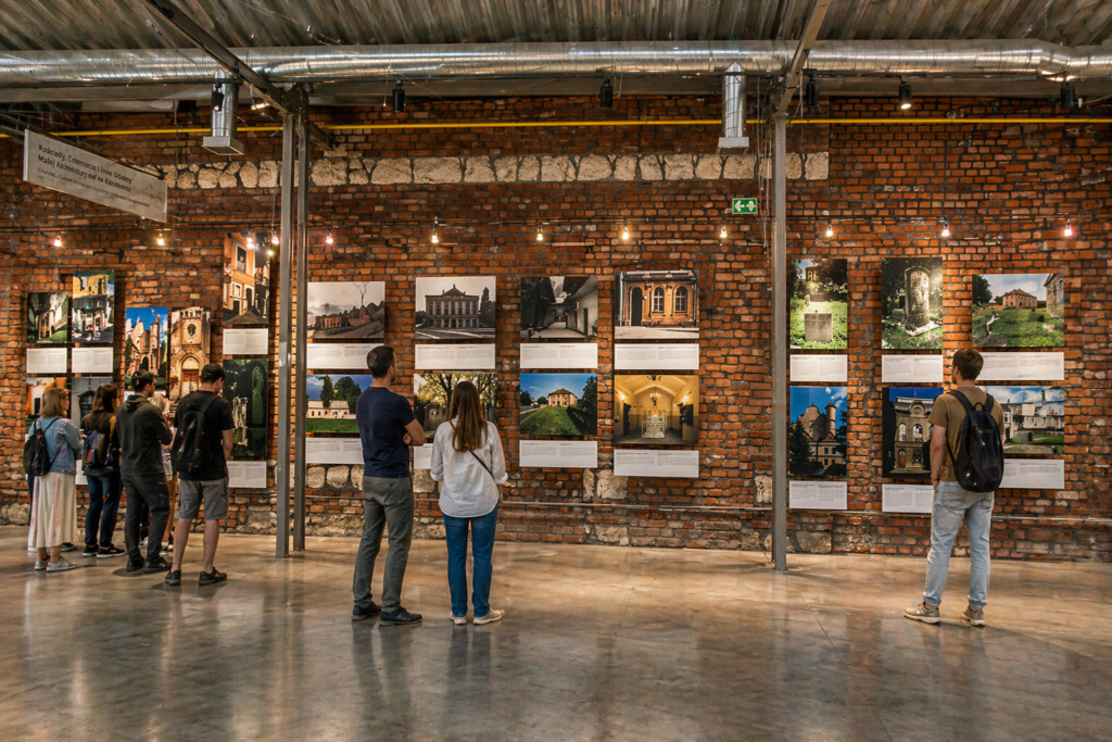 Visitors exploring an exhibition inside Galicia Jewish Museum in Krakow, with historical photographs displayed on a brick wall in an industrial-style interior.