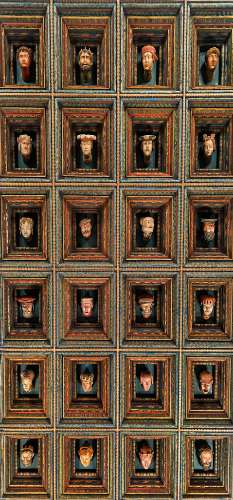 Wawel heads exhibition in Krakow showing carved wooden Renaissance ceiling heads in decorative grid.