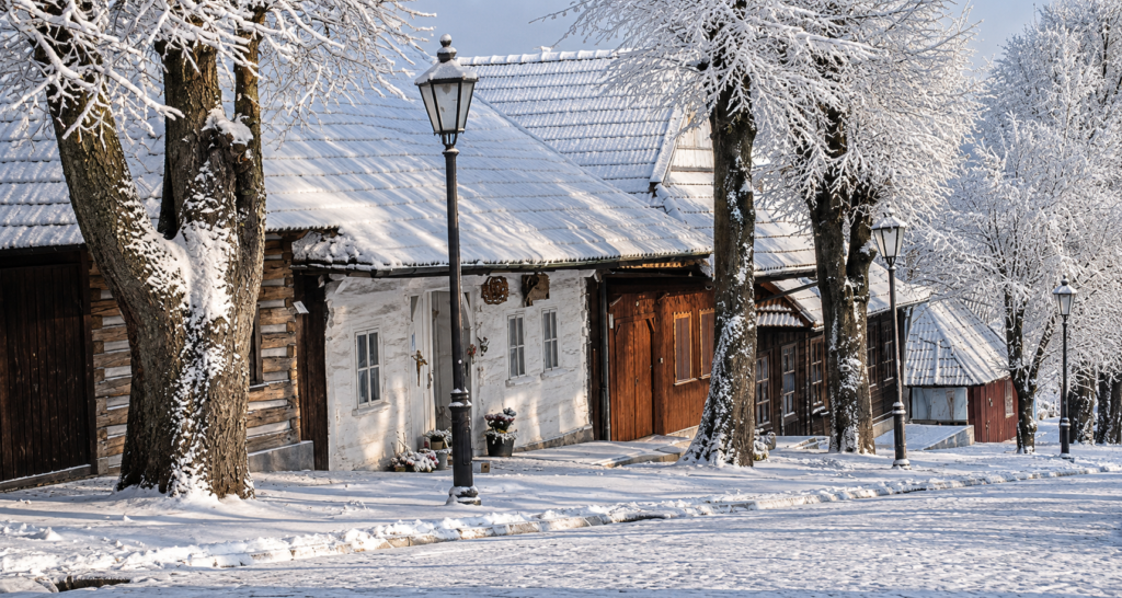 Snow-covered wooden houses and quiet village street in Lanckorona during winter in southern Poland.